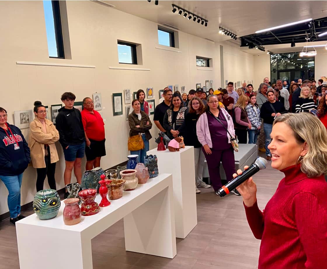 Women speaking in front of a large crowd at an art exhibit